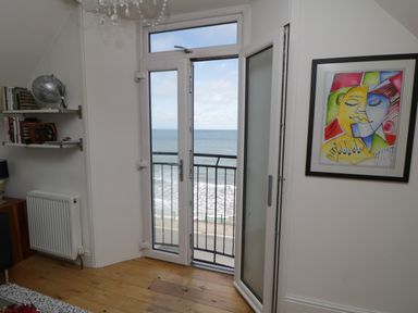 A room with wooden floor an open glass door overlooking the sea a bookshelf and framed artwork on the wall at Flat 3 Peacehaven Sandsend near Whitby