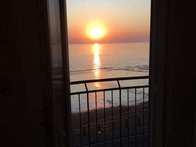 A sunset view over the ocean seen through a balcony door with a railing at Flat 3 Peacehaven in Sandsend near Whitby