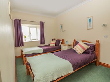 A bedroom with two single beds with purple bedding and light green throws at Sorrel Cottage in Padstow