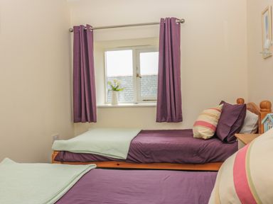 A bedroom with two single beds with purple bedding and green throws under a window with purple curtains at Sorrel Cottage in Padstow