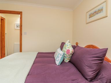 A bedroom with a bed with purple bedding and decorative pillows and a door leading to another room at Sorrel Cottage in Padstow
