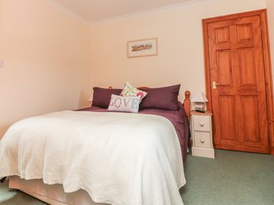 A bedroom with a bed covered with white and purple bedding and pillows with a nightstand and wooden door at Sorrel Cottage in Padstow
