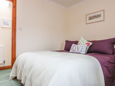 A bedroom with a bed covered with white and purple bedding and pillows with a picture on the wall at Sorrel Cottage in Padstow
