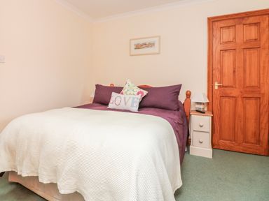 A bedroom with a double bed purple pillows and white bedspread a wooden door and a bedside table lamp at Sorrel Cottage Padstow