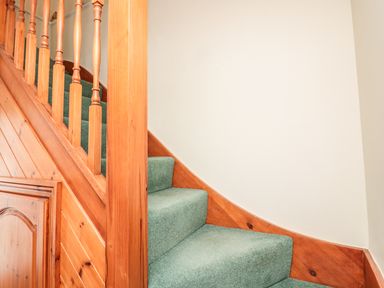 A staircase with green carpet and wooden banister in a hallway at Sorrel Cottage in Padstow