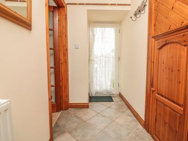 A hallway with tiled floor wooden doors and a door with a lace curtain at Sorrel Cottage in Padstow