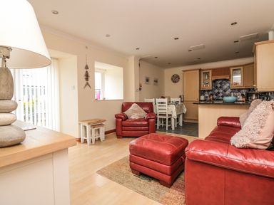 An open living room and kitchen with red leather furniture and a dining table at Sorrel Cottage in Padstow
