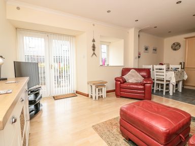 A living room with red leather armchair and ottoman wooden floor dining table with chairs and TV at Sorrel Cottage in Padstow