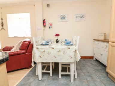 A dining area with a table set for four with blue dishes and a flower vase next to a red armchair in an open living space at Sorrel Cottage in Padstow