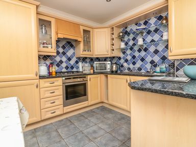 A kitchen with wooden cabinets blue tiled backsplash a built-in oven microwave and kettle at Sorrel Cottage in Padstow