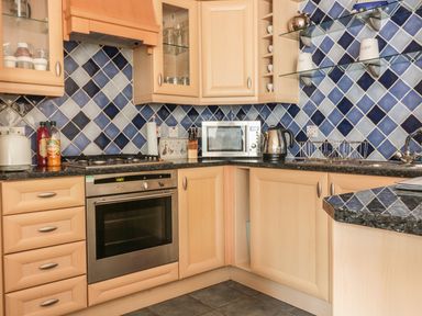A kitchen with wooden cabinets blue tiled backsplash a microwave kettle oven and countertop at Sorrel Cottage in Padstow
