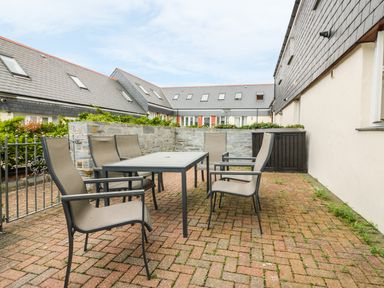 An outdoor patio with six chairs around a rectangular table and a stone wall at Sorrel Cottage in Padstow