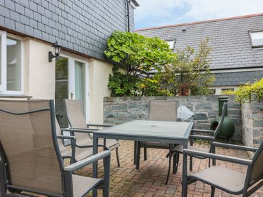 An outdoor patio with a square table and six chairs surrounded by stone walls and plants at Sorrel Cottage in Padstow