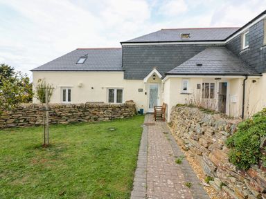 A house with beige walls a slate roof a stone wall and a grass lawn at Sorrel Cottage in Padstow