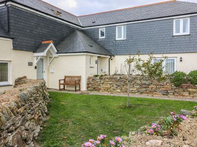 A stone wall garden with a wooden bench and a small tree outside a cottage with slate roofing at Sorrel Cottage in Padstow