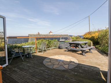 A wooden outdoor deck with chairs a round table picnic bench and plants at Blackbrae Cabin in Glenboig near Coatbridge Glasgow and Stirling