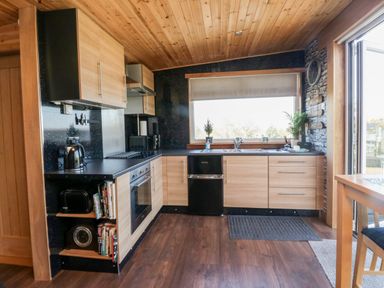 A kitchen with wooden cabinets black appliances and a large window at Blackbrae Cabin in Glenboig near Coatbridge Glasgow and Stirling