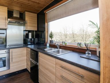 A kitchen with wooden cabinets a sink a small refrigerator and a window with outdoor view at Blackbrae Cabin in Glenboig near Coatbridge Glasgow and Stirling