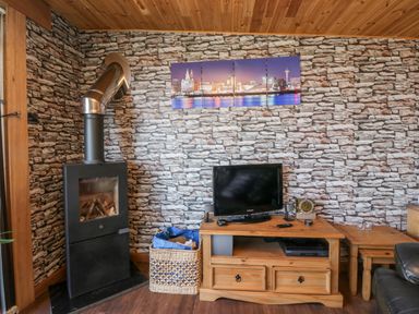 A room with a wood burning stove a basket with firewood a wooden TV stand with a television and a clock on it at Blackbrae Cabin in Glenboig near Coatbridge Glasgow and Stirling