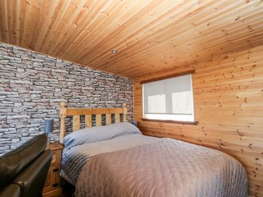 A bedroom with a wooden bedframe a quilted bedspread a nightstand with a lamp and wood paneled walls and ceiling at Blackbrae Cabin in Glenboig near Coatbridge Glasgow and Stirling