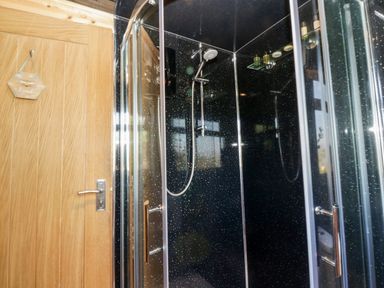 A shower enclosure with black speckled walls and a wooden door with a small hanging sign at Blackbrae Cabin in Glenboig near Coatbridge Glasgow and Stirling