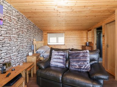 A room with a black leather sofa and two pillows a wooden bed and a stone pattern wall at Blackbrae Cabin in Glenboig near Coatbridge Glasgow and Stirling
