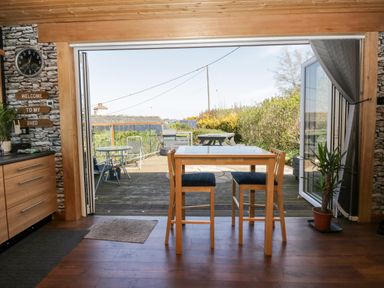 A dining area with wooden table and chairs opening to a wooden deck with outdoor furniture at Blackbrae Cabin in Glenboig near Coatbridge Glasgow and Stirling