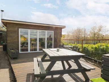 An outdoor wooden deck with a picnic table benches and a wooden cabin with glass doors at Blackbrae Cabin in Glenboig near Coatbridge Glasgow and Stirling