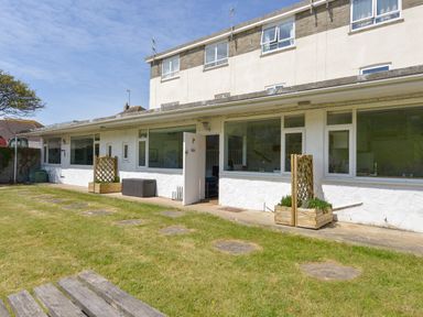 A garden area with a grass lawn and stepping stones in front of a white building with windows and an open door at 2 Brook Cottages in Hope Cove