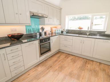 A kitchen with gray cabinets granite countertops a built in oven a sink under a window and a wooden floor at Newbiggin Cottage in Blanchland