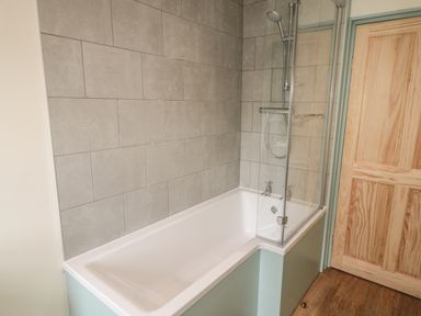 A bathroom with a bathtub shower combination next to a wooden door at Newbiggin Cottage in Blanchland