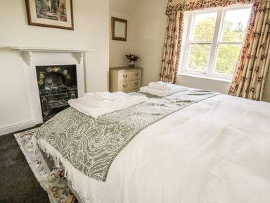 A bedroom with a bed covered with white linens and a patterned throw near a window with floral curtains at Newbiggin Cottage in Blanchland