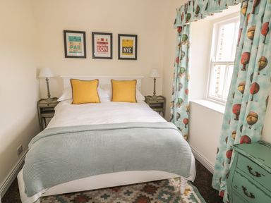 A bedroom with a double bed yellow pillows bedside tables lamps window with hot air balloon curtains and a green chest of drawers at Newbiggin Cottage in Blanchland