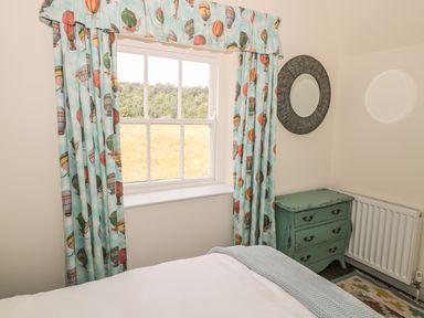 A bedroom window with hot air balloon curtains a green chest of drawers and a round wall mirror at Newbiggin Cottage in Blanchland