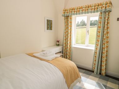 A bedroom with a bed with folded towels and a yellow blanket near a window with floral curtains at Newbiggin Cottage in Blanchland