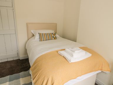 A single bed with a yellow patterned throw blanket and folded white towels in a bedroom at Newbiggin Cottage in Blanchland