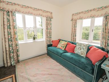 A sitting room with green sofa and floral cushions by two windows with floral curtains at Newbiggin Cottage in Blanchland