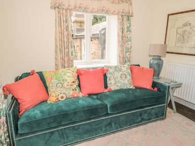A green sofa with colorful cushions near a window with patterned curtains next to a side table with a lamp at Newbiggin Cottage in Blanchland