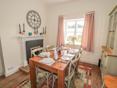 A dining room with a wooden table set for six near a window with striped curtains at Newbiggin Cottage in Blanchland