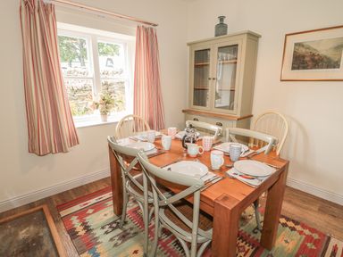 A dining room with a wooden table set for six and a cabinet with glass doors at Newbiggin Cottage in Blanchland