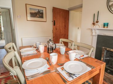 A dining table set with plates mugs and cutlery in a room with wooden door and fireplace at Newbiggin Cottage in Blanchland