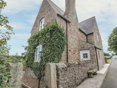 A stone cottage with ivy on the wall and a stone fence along a road at Newbiggin Cottage in Blanchland