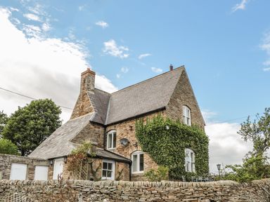 A stone house with ivy on the wall and a slate roof behind a stone wall at Newbiggin Cottage in Blanchland