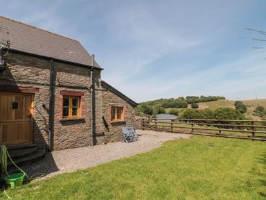 An outdoor area with a stone building and chairs at Penrhiwarwydd Barn Pontywaun