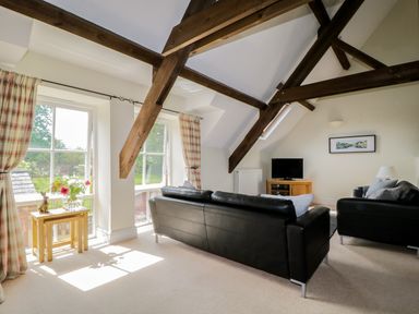 A living room with black leather sofas wooden beams and windows with curtains at Carpenters Cottage in Cockermouth