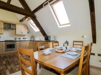 A dining table set for tea in a kitchen with wooden beams and skylight windows at Carpenters Cottage in Cockermouth