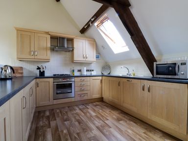 A kitchen with wooden cabinets a stove a microwave and a skylight window at Carpenters Cottage in Cockermouth