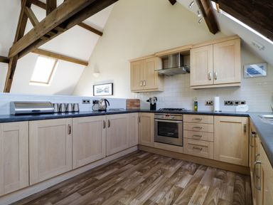 A kitchen with wooden cabinets black countertops and exposed wooden beams at Carpenters Cottage in Cockermouth