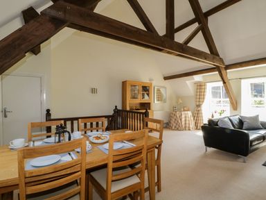 A dining area with a wooden table and chairs set for tea and a sitting area with a black sofa under exposed wooden beams at Carpenters Cottage in Cockermouth