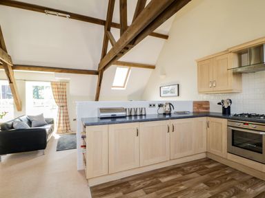 A kitchen with wooden cabinets and black countertop next to a living area with a black sofa and checked curtains at Carpenters Cottage in Cockermouth